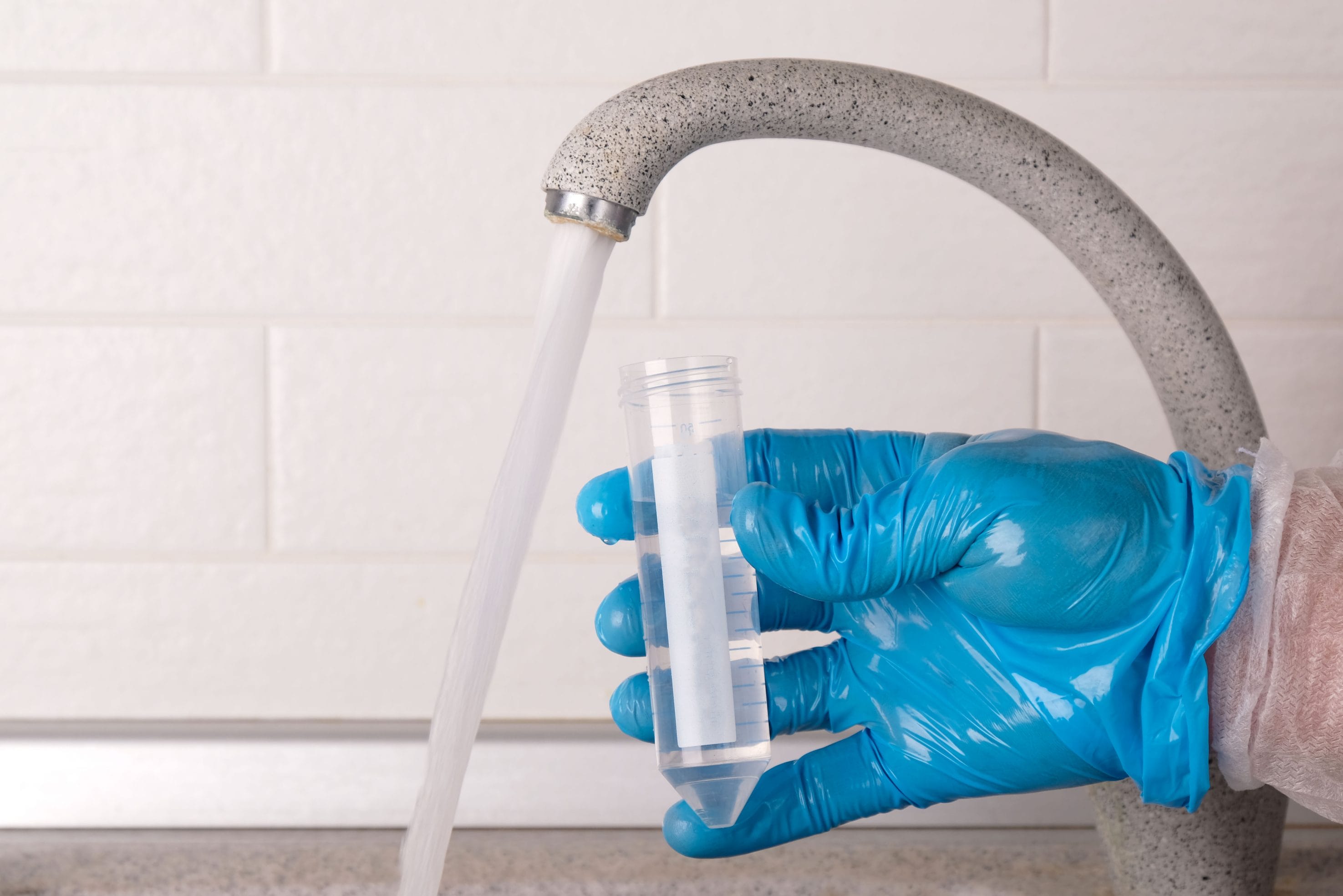 Gloved Hand Collecting Water Sample from Faucet for Commercial Quality Testing
